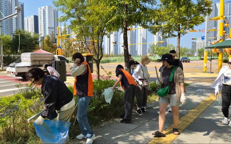 참여자들이 마을 생활도로와 녹지에서 쓰레기를 수거하며 주변을 정비하고 있다.