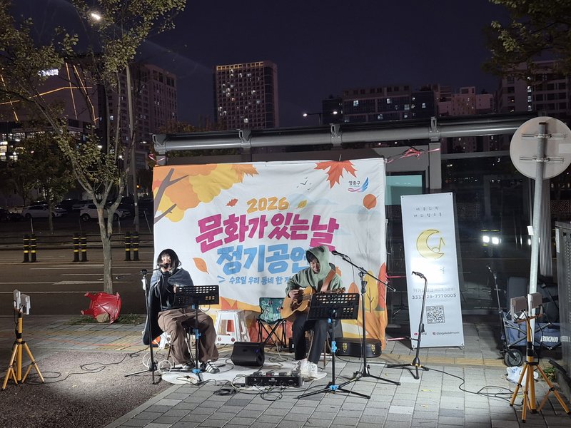 21일 저녁 운서역 2번 출구 버스정류장 앞에서 공연단체 ‘조각달’이 기타 연주와 함께 라이브 공연을 하고 있다.